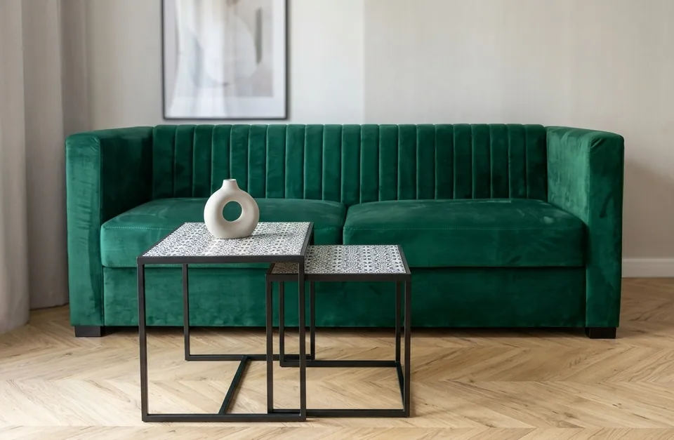 Zielona tapicerowana sofa za dwoma stolikami na czarnych stelażach